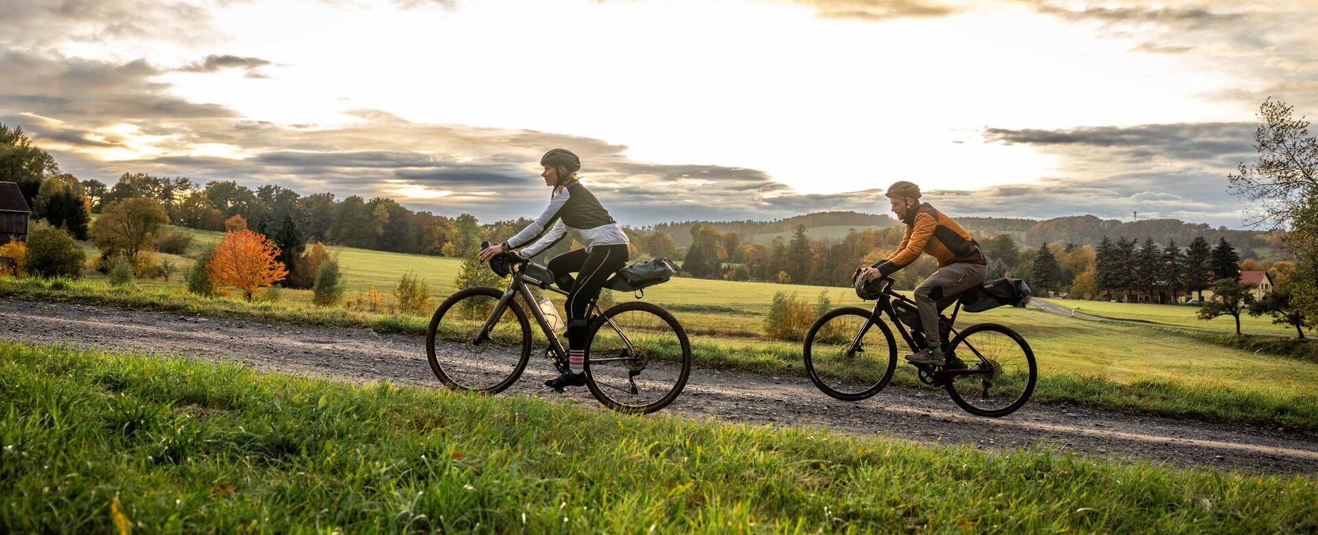 Dva gravel bikeři jedou do kopce na RockHead, povrch je štěrkový, v pozadí je vidět obec Rosenthal, je podzim.