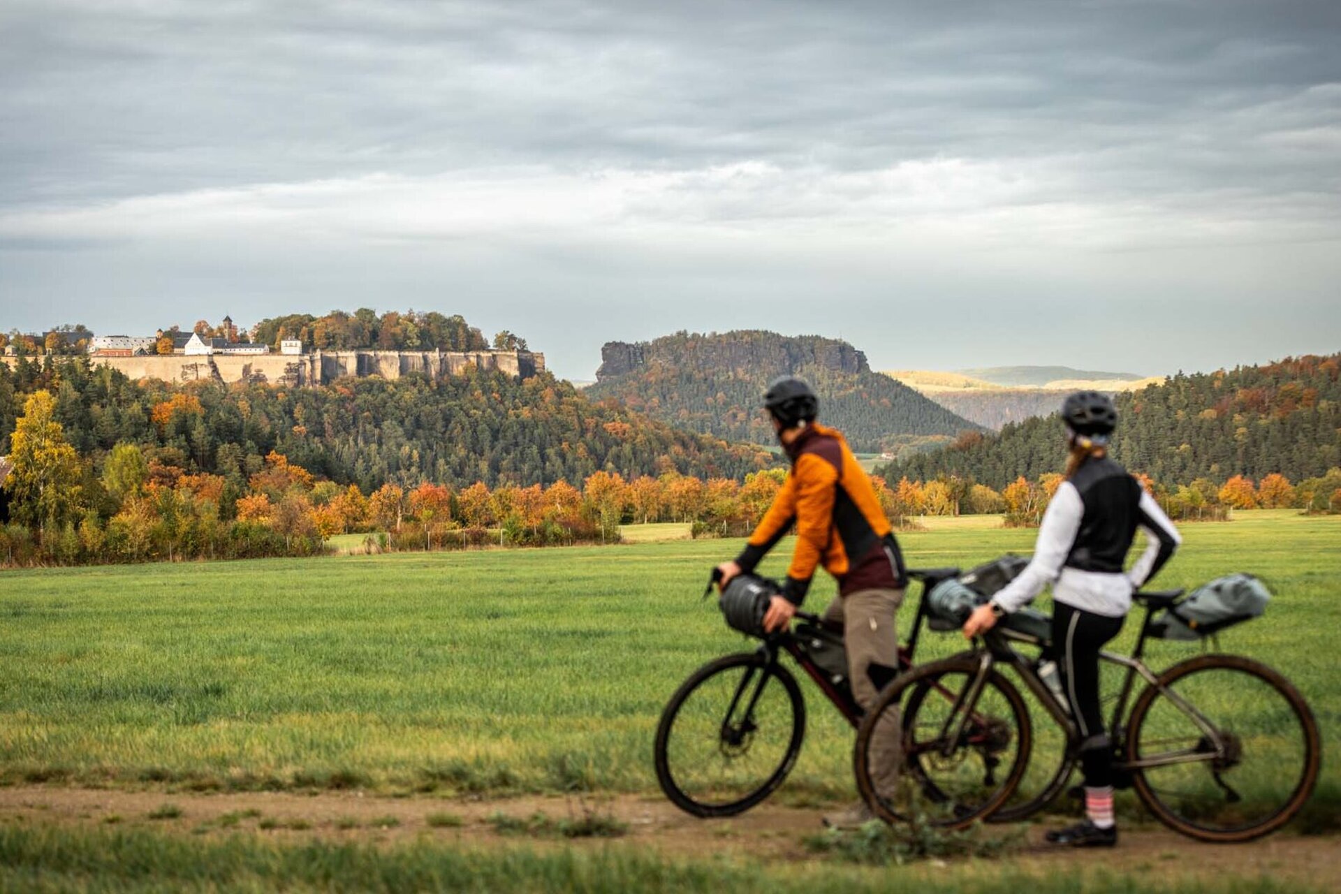 Dva gravel bikeři na RockHead na žluté rychlostní zkoušce se dívají na pevnost Königstein a Lilienstein v dálce.